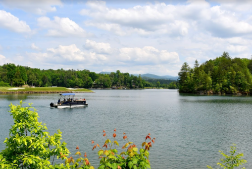 A serene lake scene with a boat on the water, surrounded by lush greenery and distant mountains under a cloudy sky.