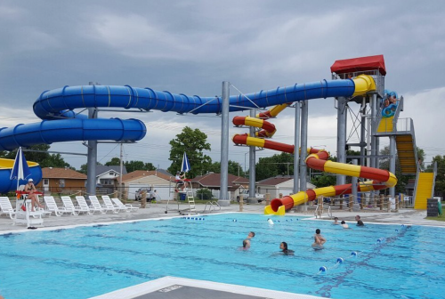 A water park featuring a large blue and red waterslide next to a swimming pool with people enjoying the water.