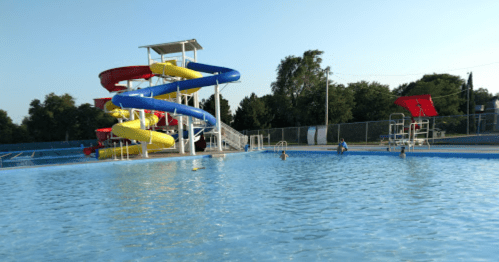 A sunny pool scene featuring colorful water slides and children playing in the water.