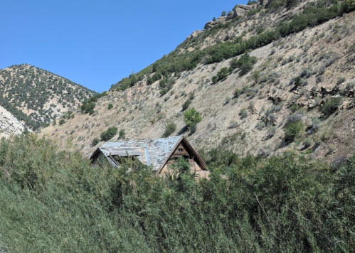 An old, weathered cabin nestled among green grass and hills under a clear blue sky.