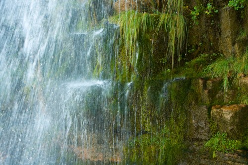 A close-up of a waterfall cascading over moss-covered rocks, with water droplets glistening in the sunlight.
