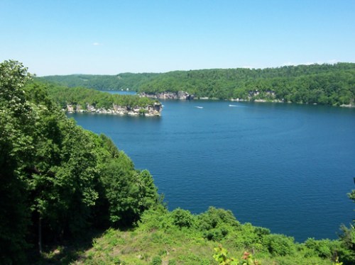 A serene lake surrounded by lush green hills under a clear blue sky.