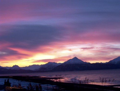 A stunning sunset over snow-capped mountains, with vibrant pink and purple skies reflecting on the water.