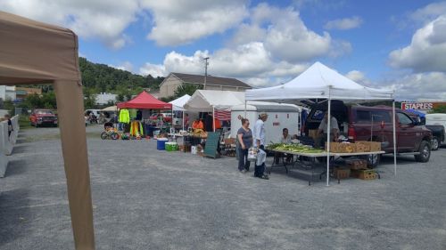 A bustling outdoor market with various tents, vendors, and shoppers under a partly cloudy sky.