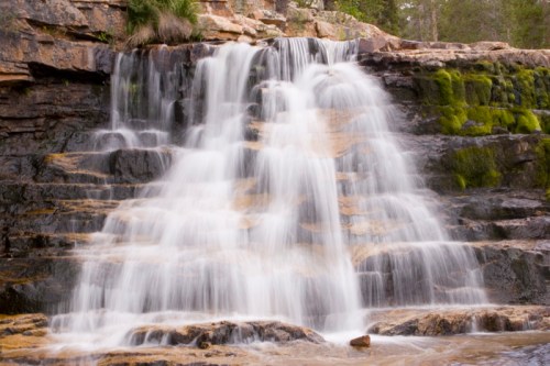 A serene waterfall cascading over rocky terrain, surrounded by lush greenery and moss.