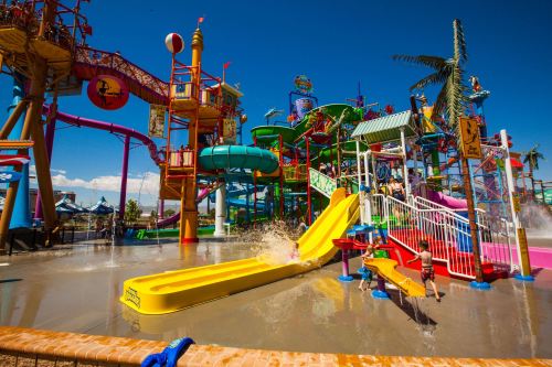 Colorful water park with slides, pools, and playful structures under a clear blue sky. Kids enjoying the water.