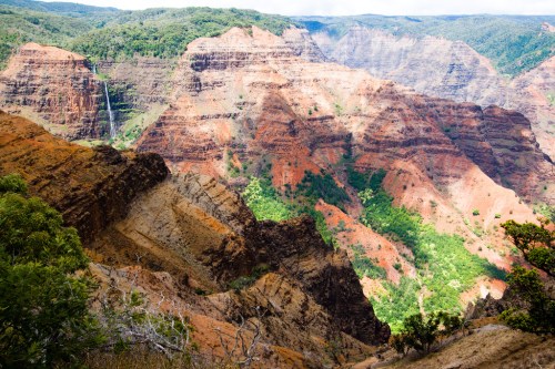 A vibrant landscape of steep, colorful canyon walls with lush greenery and a waterfall in the distance.