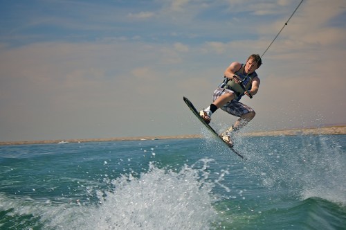 A person performs a jump while wakeboarding on a sunny day, with splashes of water around them.