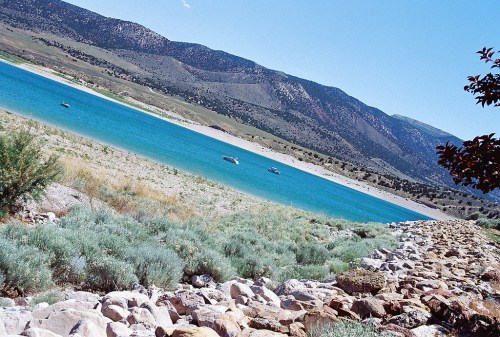 A serene lake surrounded by green hills and rocky shores, with boats gently floating on the turquoise water.