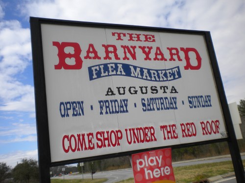 Sign for "The Barnyard Flea Market" in Augusta, open Friday to Sunday, inviting shoppers to "come shop under the red roof."