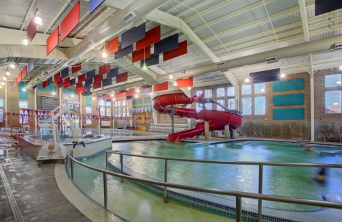 Indoor swimming pool with a red water slide, diving board, and colorful banners hanging from the ceiling.