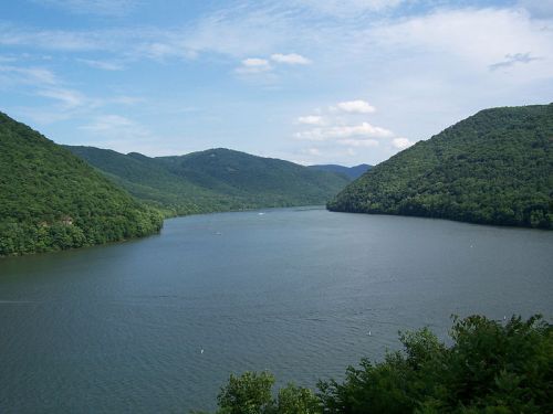 A serene lake surrounded by lush green mountains under a partly cloudy sky.