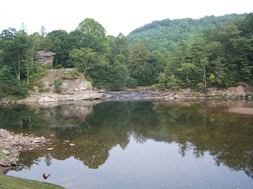 A serene lake surrounded by lush green trees and rocky formations, reflecting the landscape in calm waters.