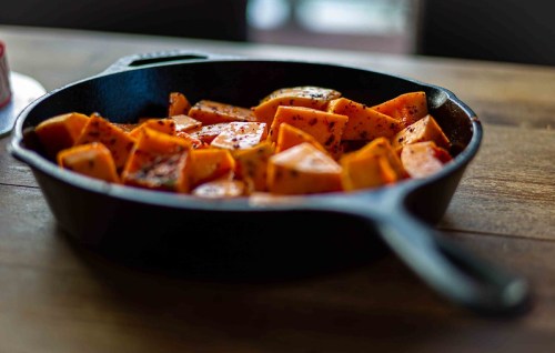 A cast iron skillet filled with seasoned, cubed butternut squash on a wooden table.