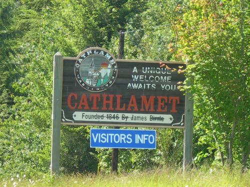 Sign welcoming visitors to Cathlamet, founded in 1846, with a "Visitors Info" section below. Surrounded by greenery.