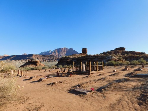 Desert landscape with a wooden structure, surrounded by rocky formations and sparse vegetation under a clear blue sky.