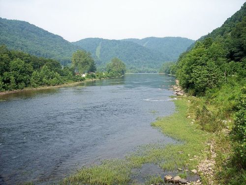 A serene river flows through lush green hills, with trees lining the banks and a calm atmosphere.