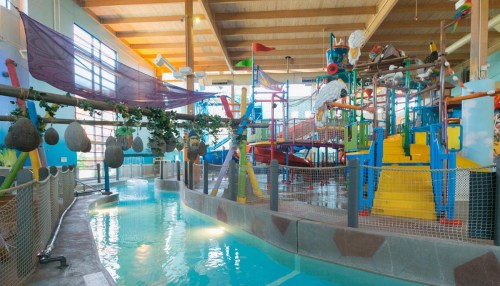 Colorful indoor water play area with slides, climbing structures, and a shallow pool. Bright and inviting atmosphere.