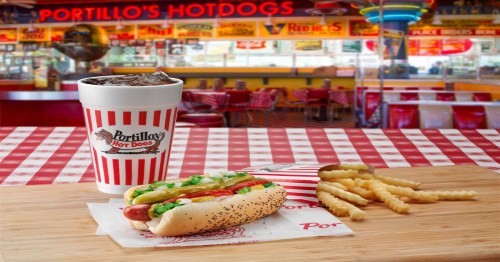 A hot dog with toppings, fries, and a drink on a checkered table in a vibrant fast-food restaurant setting.