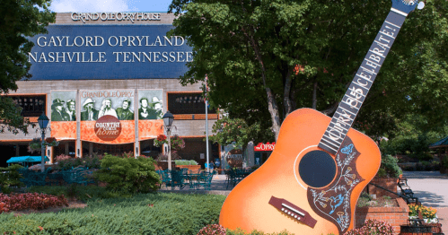 A large guitar sculpture in front of the Grand Ole Opry House in Nashville, Tennessee, surrounded by greenery and flowers.