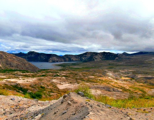 A panoramic view of a rugged landscape with mountains, a lake, and overcast skies.