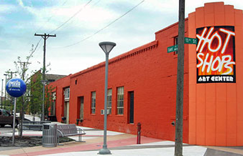 Vibrant orange building with "Hot Shops Art Center" sign, street lamps, and benches in a city setting.