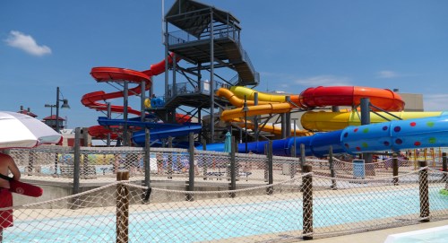Colorful water slides and a pool area under a clear blue sky, with a lifeguard station in the foreground.