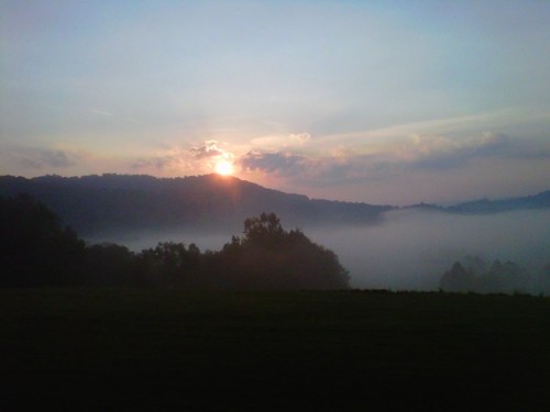A serene sunrise over misty hills, with soft clouds and a tranquil landscape.