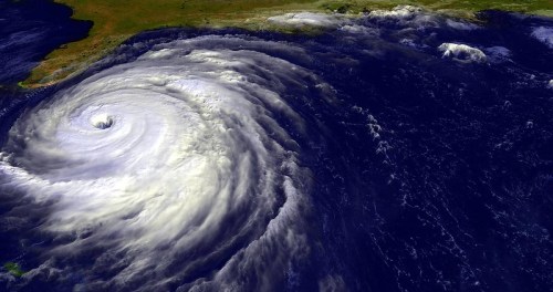 Satellite view of a powerful hurricane swirling over the ocean, with clouds and land visible in the background.