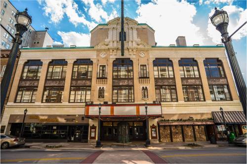 Historic theater building with ornate architecture, large windows, and a marquee, set against a blue sky.