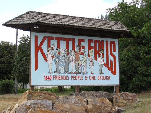 Sign for Kettle Falls featuring cartoon characters with the text "1640 Friendly People & One Grouch."