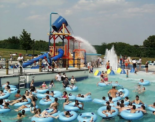 A busy water park scene with people in blue inner tubes, a large water slide, and splashing water in the background.