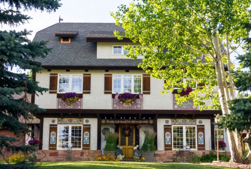 A charming multi-story house with decorative windows, flower boxes, and lush greenery surrounding it.