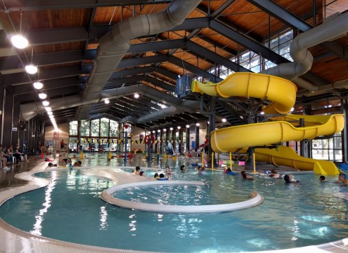 Indoor swimming pool with a yellow water slide, children swimming, and a spacious, bright environment.