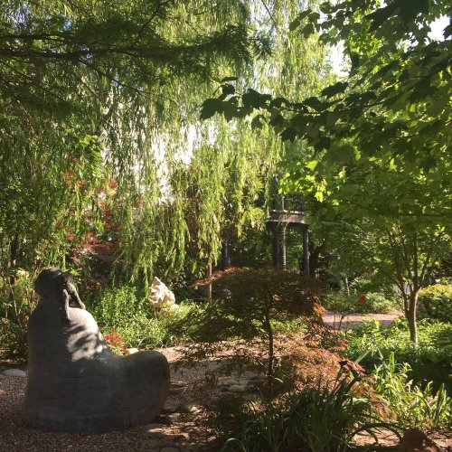 A serene garden scene featuring lush greenery and a stone sculpture nestled among plants and trees.