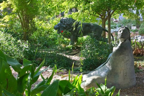 A serene garden scene featuring a lion statue and a seated figure among lush greenery.