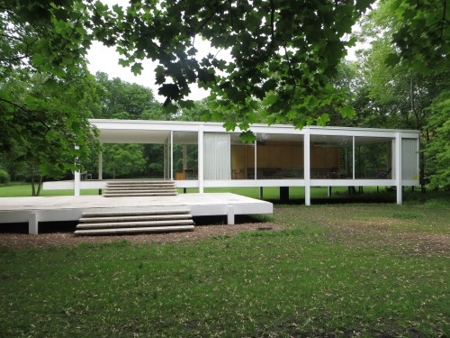 A modernist building with large glass windows, surrounded by greenery and featuring a raised platform entrance.