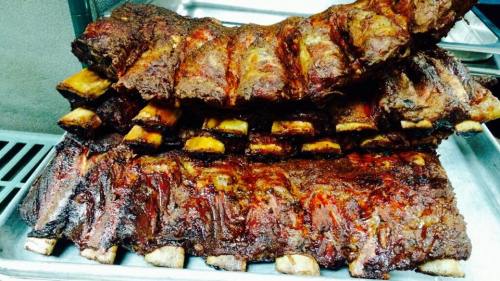 A close-up of succulent, grilled ribs stacked on a tray, showcasing a rich, smoky glaze and tender meat.