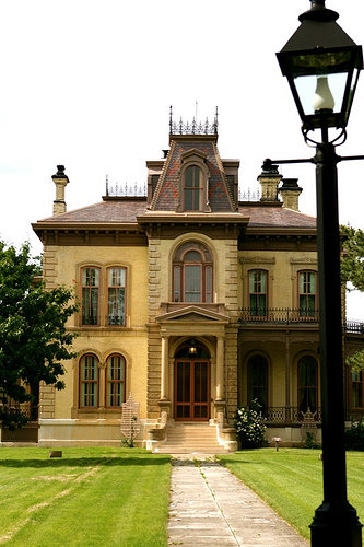A grand, historic mansion with ornate architecture, surrounded by greenery and a lamp post in the foreground.