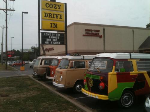 A row of vintage Volkswagen vans parked outside Cozy Drive In, with a sign advertising hot dogs.
