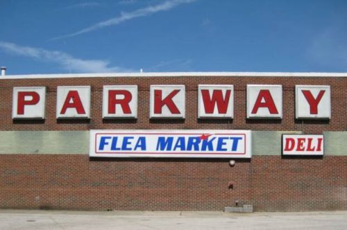 Sign on a brick building displaying "PARKWAY," "FLEA MARKET," and "DELI" against a clear blue sky.