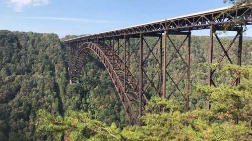 A large metal arch bridge spans a lush green valley under a clear blue sky.