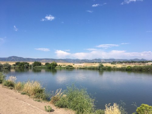 A serene river scene with lush greenery, under a clear blue sky and distant mountains.
