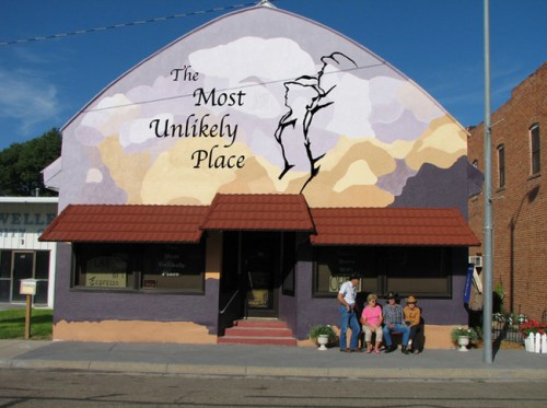 A colorful mural on a building reads "The Most Unlikely Place," with people sitting on the steps in front.