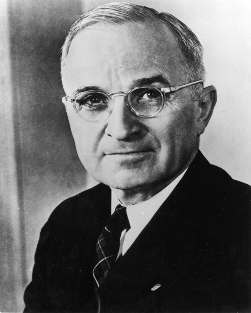 Black and white portrait of a man in glasses, wearing a suit and tie, looking directly at the camera.