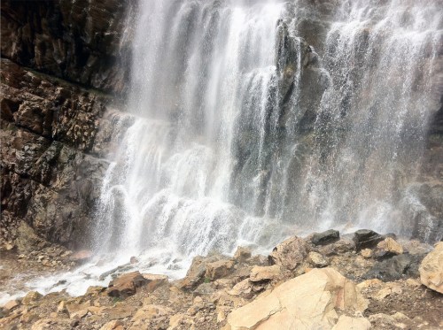 A cascading waterfall flows over rocky cliffs, surrounded by stones and natural terrain.