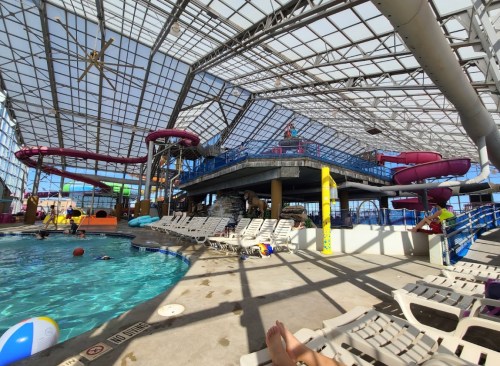 Indoor water park featuring a pool, water slides, and lounge chairs under a large glass roof.