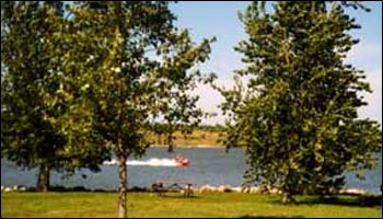 A scenic view of a lake with a boat speeding by, framed by lush green trees on the shore.
