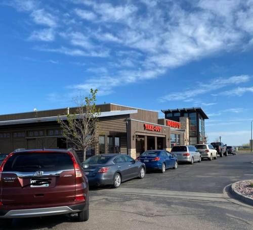 A line of cars waiting at a take-out restaurant under a clear blue sky.