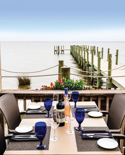 A scenic waterfront dining setup with blue glasses, plates, and a view of a pier extending into the water.
